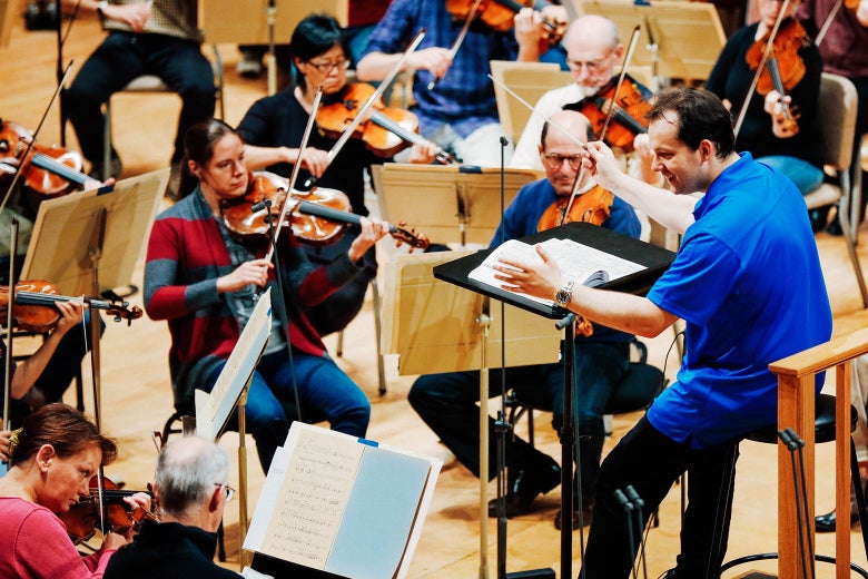 Musicians play stringed instruments as a man directs.
